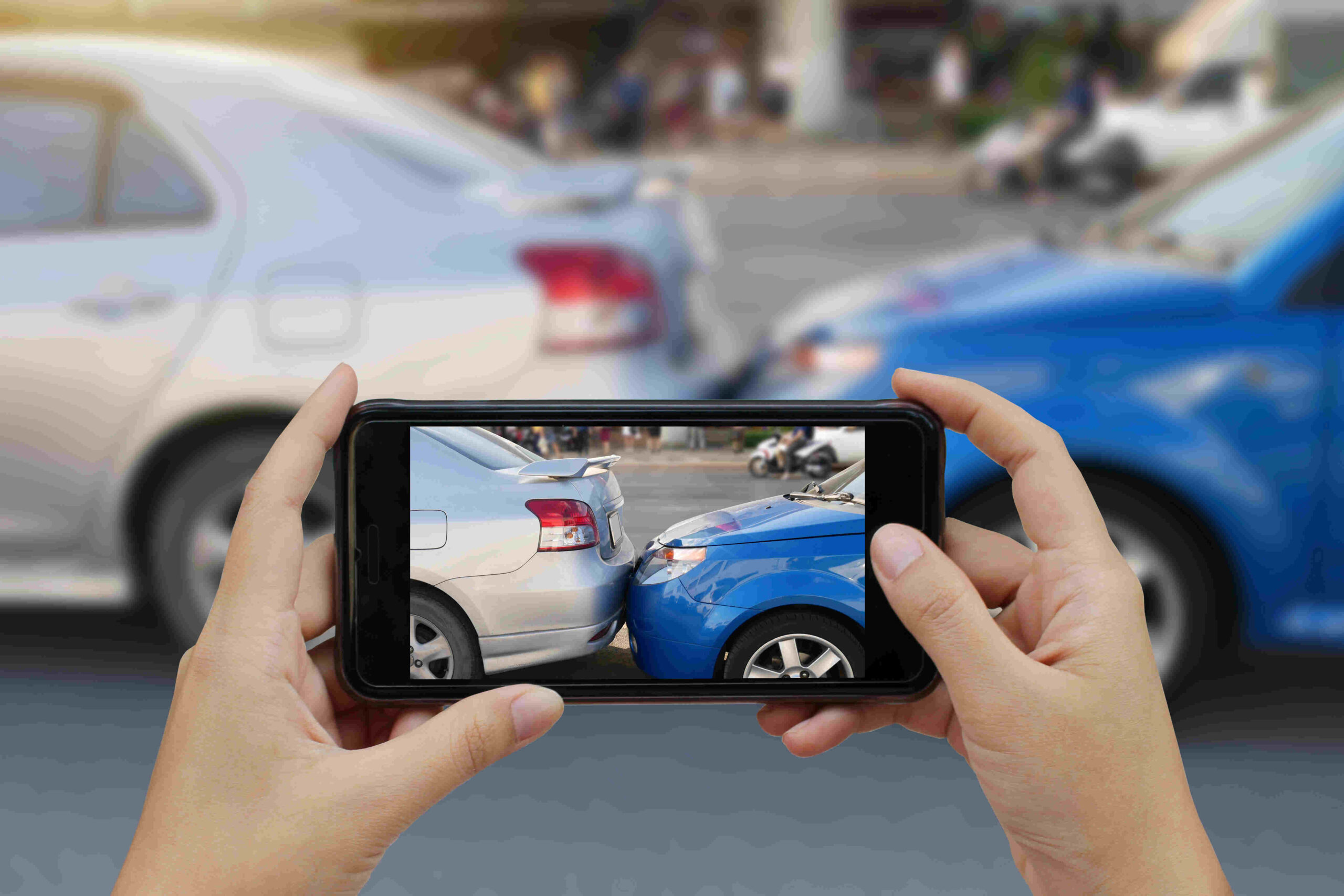 Image of a phone camera taking a picture of a silver car being rear-ended by a blue car.