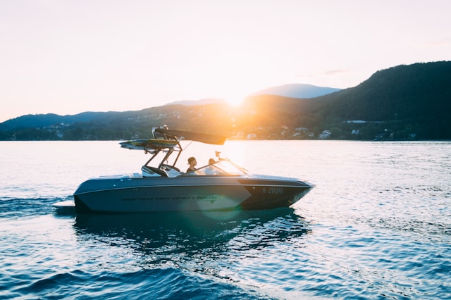 A boat on a lake with some mountains and the sun in the background.