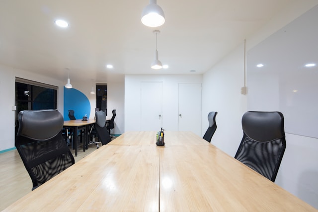 An office space with a large conference desk and black office chairs surrounding it.