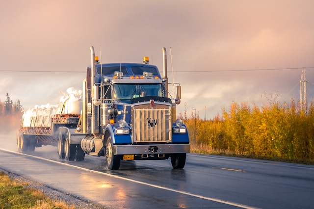 Blue semi-truck driving on the road with trees in the background.