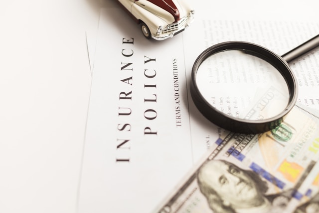 Image of sheet of paper with "insurance policy terms and conditions" written on it next to a magnifying glass, a one hundred dollar bill, and a toy car.