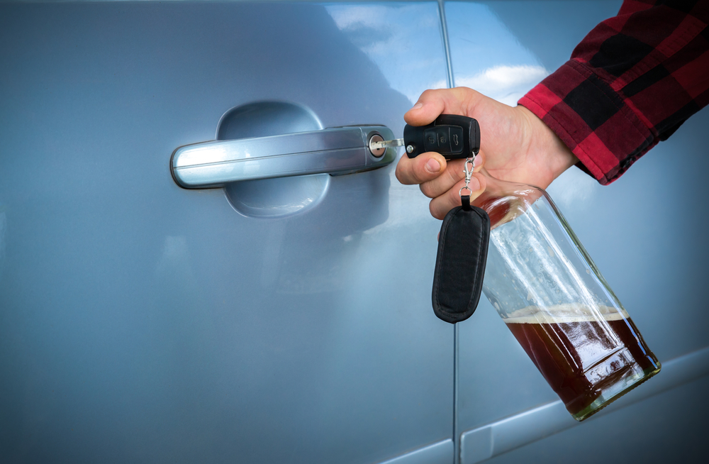 A person holding a car key and a partly filled alcohol bottle while opening a vehicle door, showing the kind of risky behavior often at the center of Missouri Drunk Driving Cases.