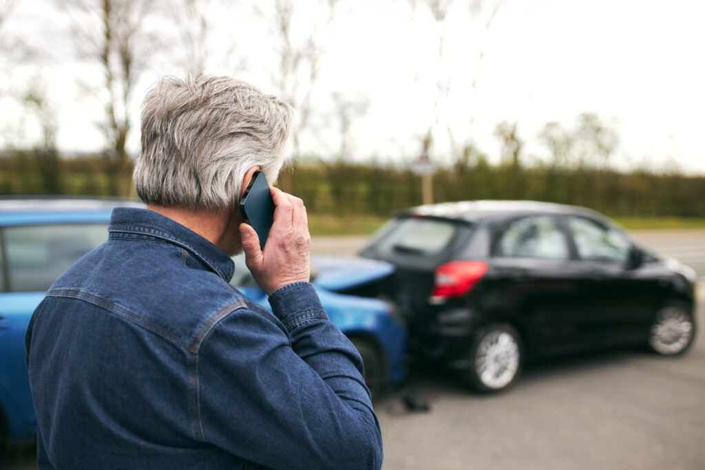 Older man calling for help at the scene of a rear end collision with two damaged cars, illustrating the stress and confusion after an uninsured driver hit me in Kansas.