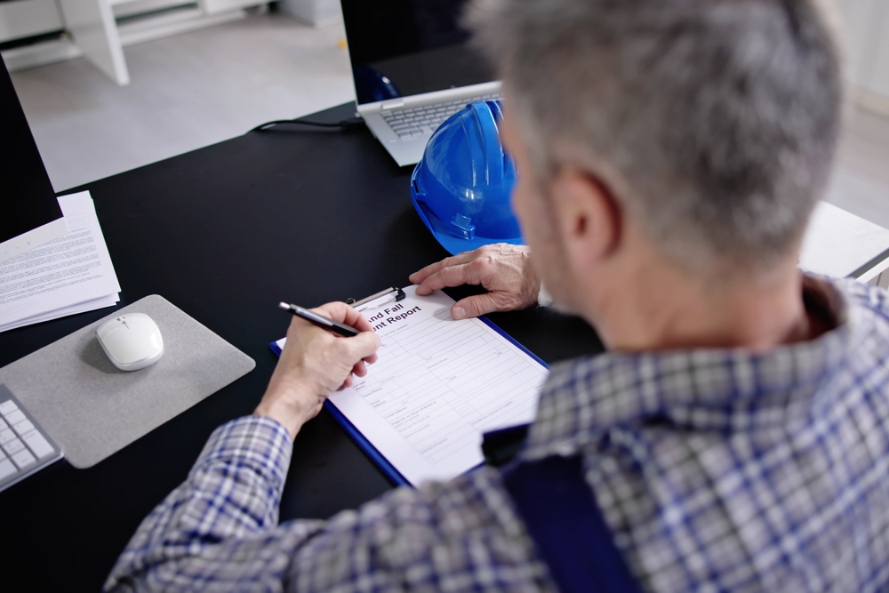 An injured worker filling out an incident report at a desk with a hard hat nearby, reflecting the process often involved when someone is fired while on workers’ comp.