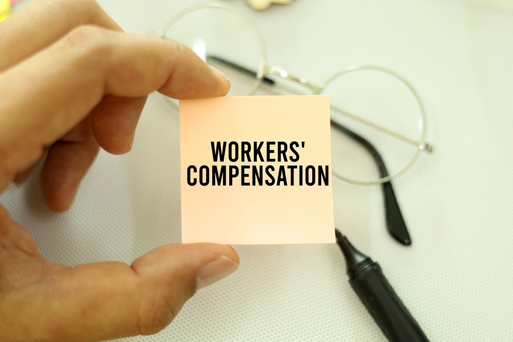 A person holding a note that says “Workers' Compensation,” highlighting paperwork concerns often involved in dual jurisdiction benefits cases.