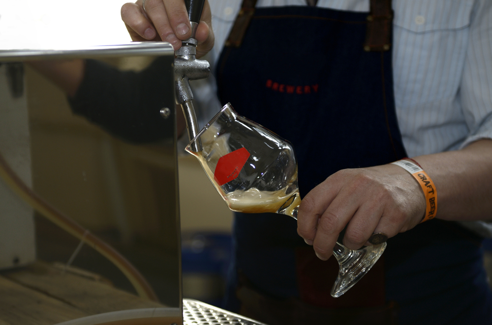 Bartender’s hands pouring a glass with draught beer from a beer tower.
